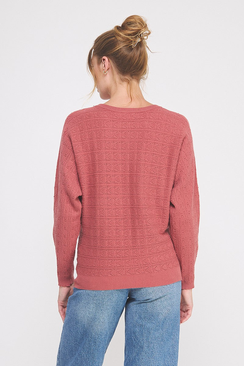 Person wearing a pink sweater with a subtle pattern on a white background