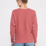 Person wearing a pink sweater with a subtle pattern on a white background