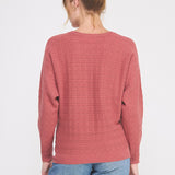 Person wearing a pink sweater with a subtle pattern on a white background