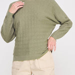 Woman wearing a green sweater and beige pants on a white background