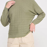 Woman wearing a green sweater and beige pants on a white background