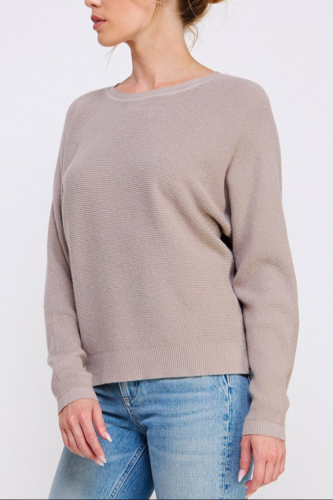 Woman wearing a beige sweater and blue jeans on a white background