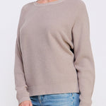 Woman wearing a beige sweater and blue jeans on a white background