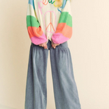 Person wearing a colorful sweater and wide-leg jeans on a plain background