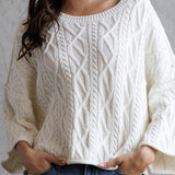 Person wearing a white cable knit sweater and blue jeans against a gray background