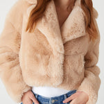 Person wearing a beige faux fur jacket and blue jeans on a white background