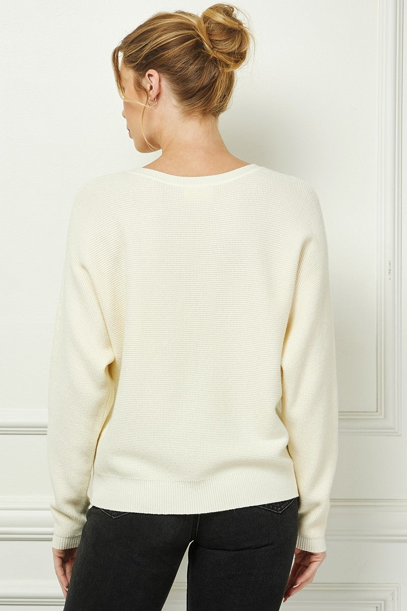 Woman wearing a cream sweater against a white wall