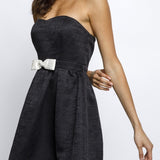 Woman wearing a black strapless dress with a white belt on a white background