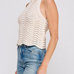 Woman wearing a beige sleeveless knitted top and blue jeans on a white background