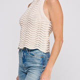 Woman wearing a beige sleeveless knitted top and blue jeans on a white background