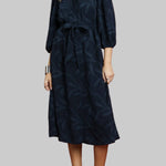 Woman wearing a navy dress with a subtle pattern on a red background