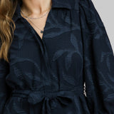 Woman wearing a navy blue dress with leaf pattern against a red background