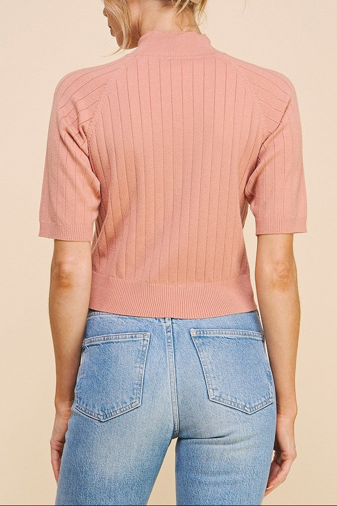 Person wearing a pink ribbed sweater and blue jeans on a beige background