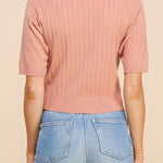 Person wearing a pink ribbed sweater and blue jeans on a beige background