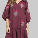 Woman wearing a plum dress with floral embroidery on a white background