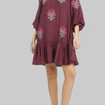 Woman wearing a burgundy dress with floral embroidery on a gray background