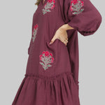 Woman wearing a plum dress with floral embroidery on a white background