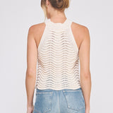 Woman wearing a white sleeveless knitted top and blue jeans on a light gray background