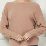 Woman wearing a brown sweater and blue jeans against a white wall