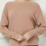 Woman wearing a brown sweater and blue jeans against a white wall