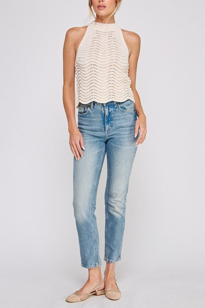Woman wearing a white sleeveless top and blue jeans on a light gray background