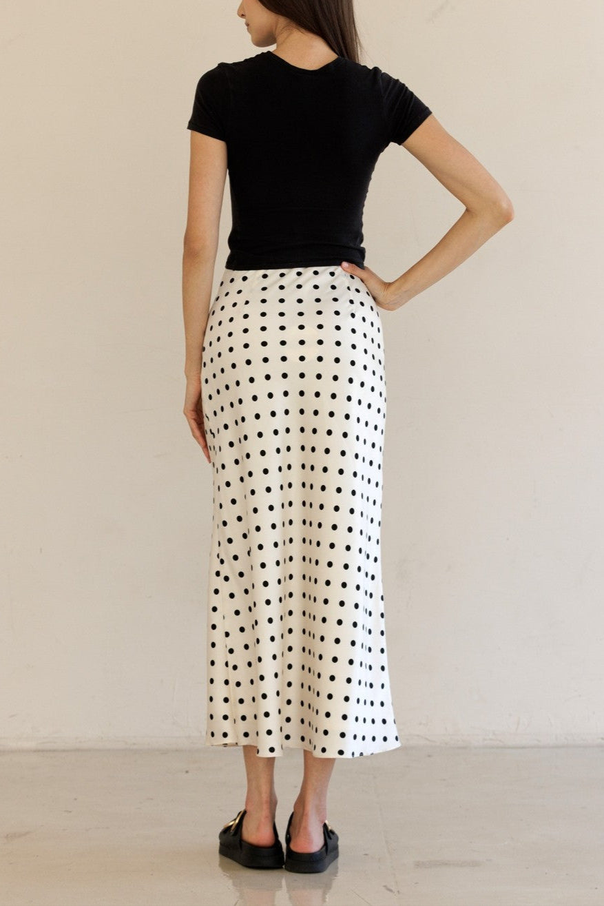 Woman wearing a black t-shirt and white polka dot skirt against a beige background
