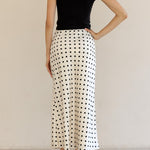 Woman wearing a black t-shirt and white polka dot skirt against a beige background