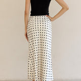 Woman wearing a black t-shirt and white polka dot skirt against a beige background