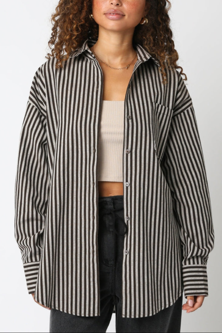 Woman wearing a black and white striped shirt over a beige top and black pants on a white background