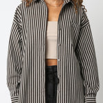 Woman wearing a black and white striped shirt over a beige top and black pants on a white background