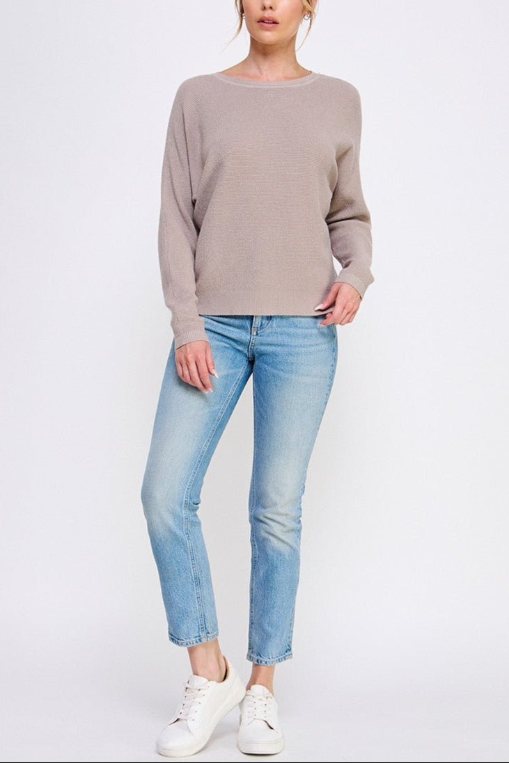 Woman wearing a beige sweater and light blue jeans on a white background
