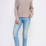 Woman wearing a beige sweater and light blue jeans on a white background