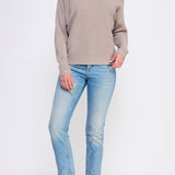 Woman wearing a beige sweater and light blue jeans on a white background