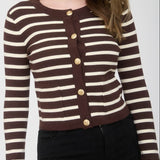 Woman wearing a brown and white striped cardigan with gold buttons on a plain background