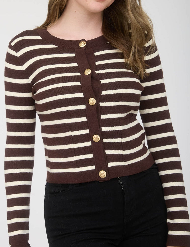 Woman wearing a brown and white striped cardigan with gold buttons on a plain background