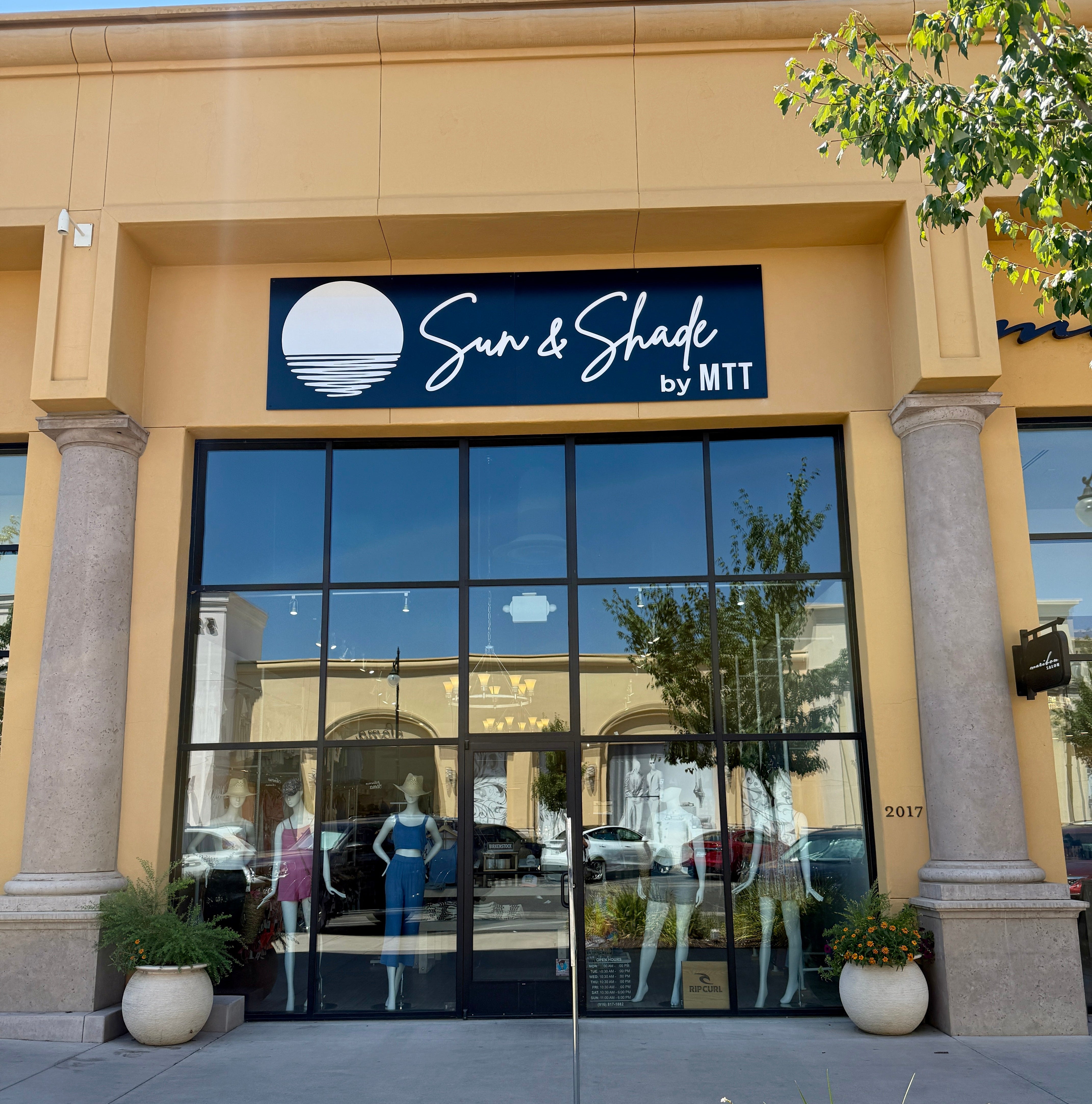 Storefront of 'Sun & Shade by MTT' with glass doors and visible interior.