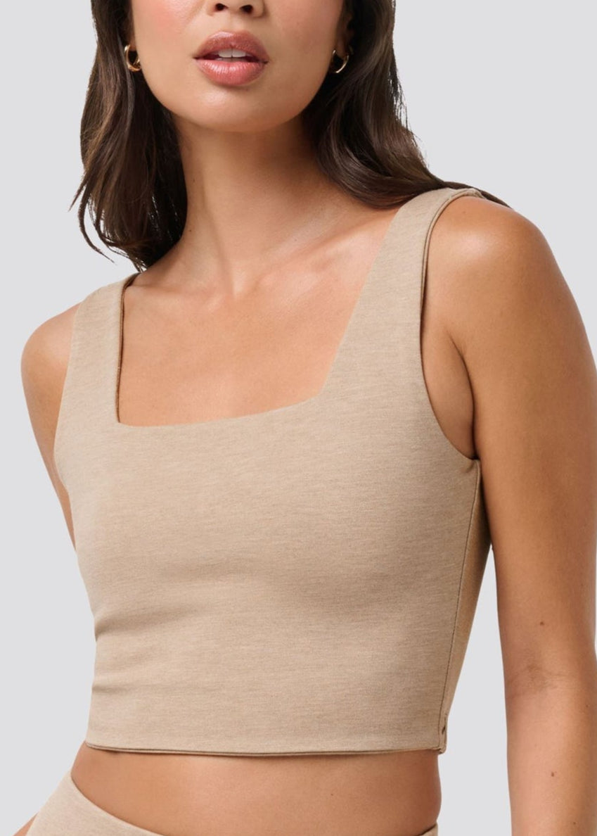 Woman wearing a beige tank top against a plain background