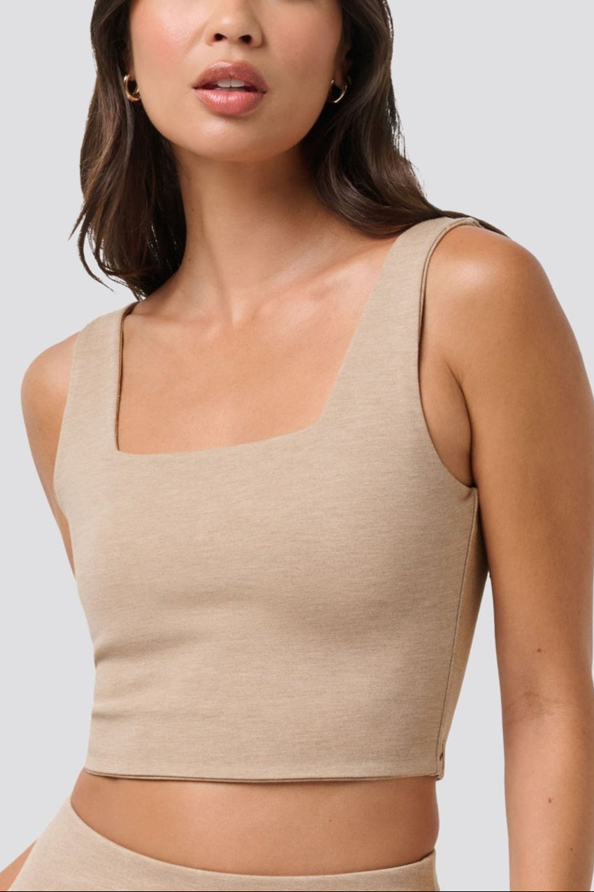 Woman wearing a beige tank top against a plain background
