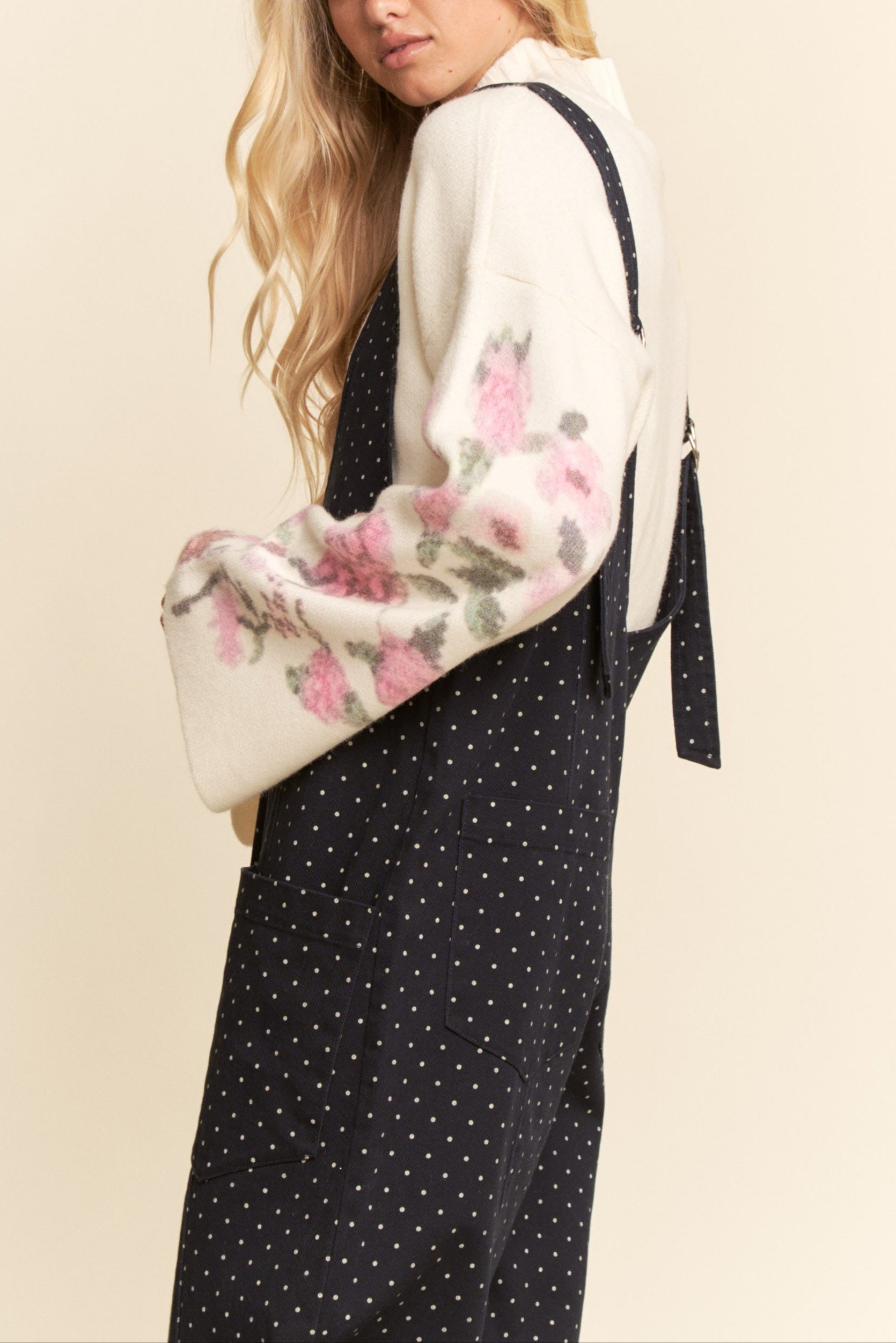 Woman wearing a floral blouse and black polka dot dress on a beige background