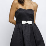 Woman wearing a black strapless dress with a white bow on a white background
