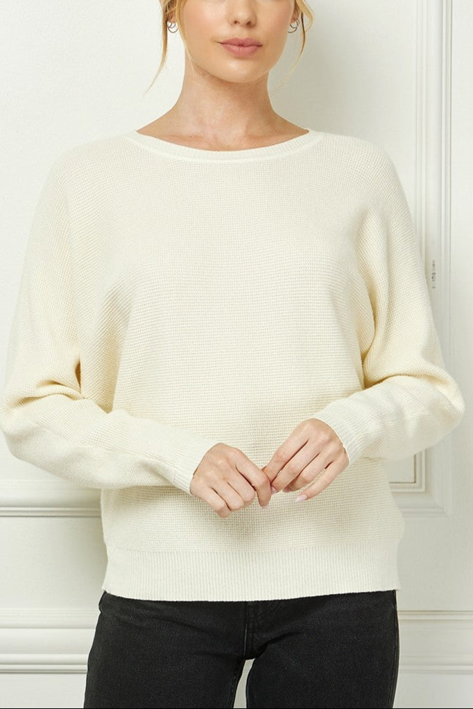 Woman wearing a cream sweater against a white wall