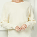 Woman wearing a cream sweater against a white wall