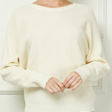 Woman wearing a cream sweater against a white wall