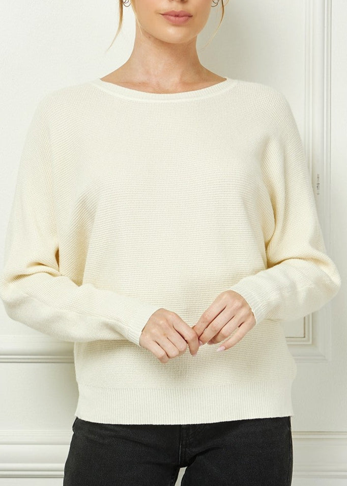Woman wearing a cream sweater against a white wall