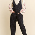 Woman wearing a polka dot jumpsuit with floral sleeves against a beige background