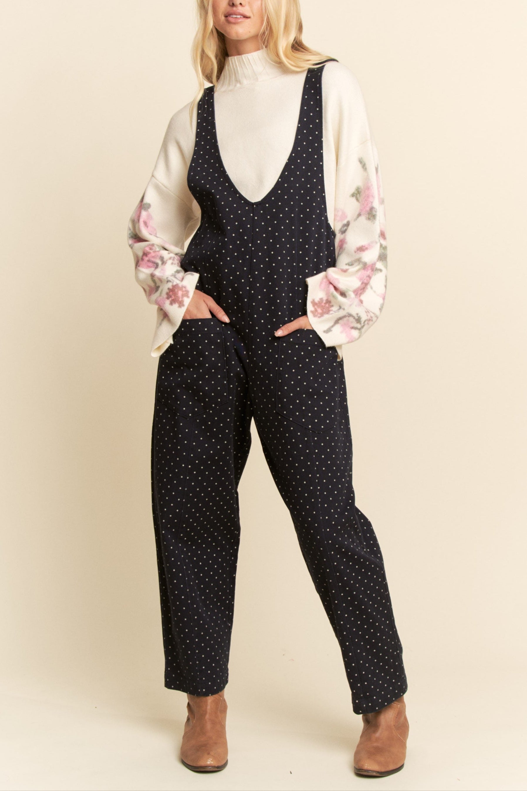 Woman wearing a polka dot jumpsuit with floral sleeves against a beige background