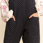 Black polka dot jumpsuit worn by a person with a floral-patterned garment in the background.