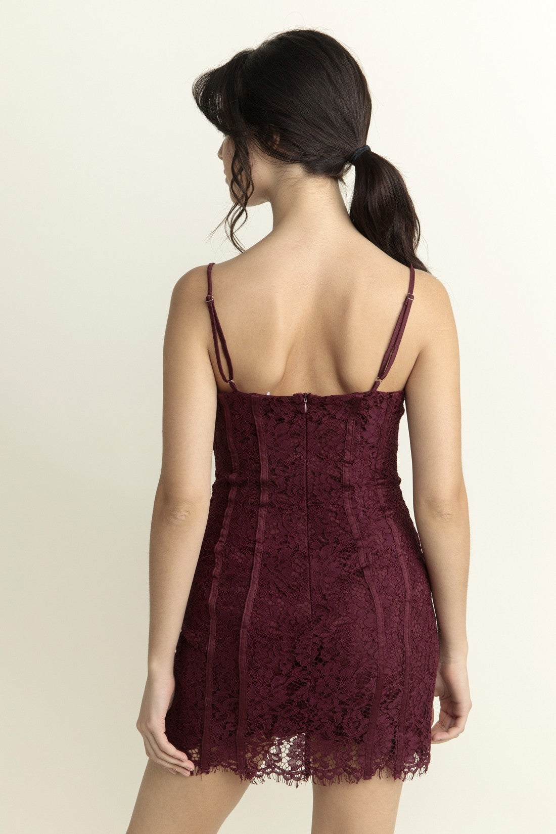 Woman wearing a burgundy lace dress against a beige background