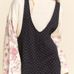 Woman wearing a black polka dot jumpsuit with a floral kimono over her shoulder on a beige background