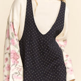 Woman wearing a black polka dot jumpsuit with a floral kimono over her shoulder on a beige background